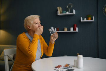 Mature grey-haired woman taling medical pills