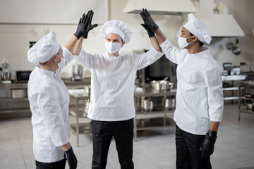 Multiracial team of chefs giving five with hands cheering each other before a job on kitchen. Concept of success and teamwork at restaurant. Idea of preparation for the cooking process in professional