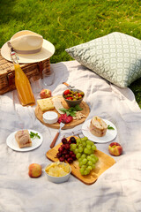 leisure, food and drinks concept - close up of snacks and picnic basket on blanket on grass at summer park