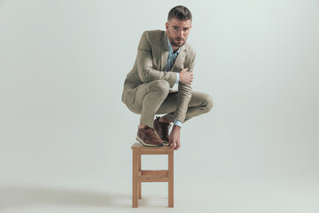 handsome businessman in squatting position posing on wooden chair