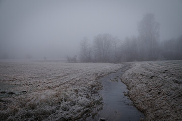 small river on a farming field on a misty cloudy winter day