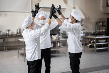 Multiracial team of chefs giving five with hands cheering each other before a job on kitchen. Concept of success and teamwork at restaurant. Idea of preparation for the cooking process in professional