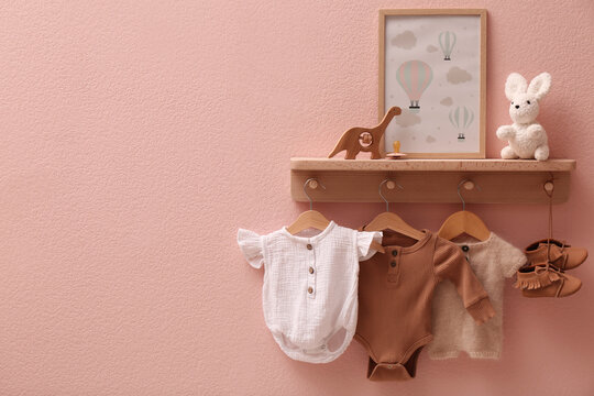 Wooden rack with cute baby clothes, shoes, toys and picture on pink wall indoors. Space for text