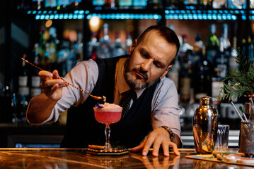 Barman is making cocktail at night club.