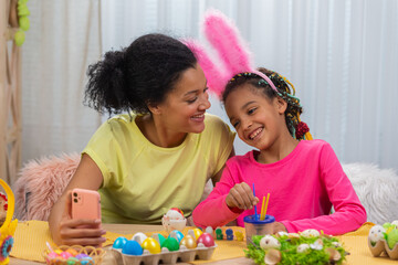 Mom and daughter with funny bunny ears talk on a video call using the phone. African American woman...