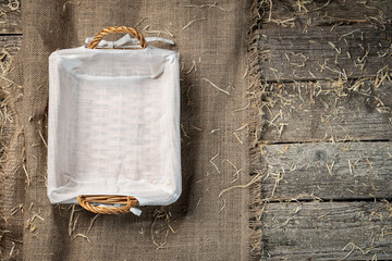 Empty wicker bread basket with white napkin on burlap cloth covered with straw or hay. Rustic...