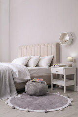 Stylish bedroom interior with knitted pouf and furniture