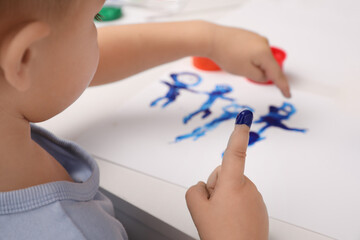Little boy painting with finger at white table indoors, closeup
