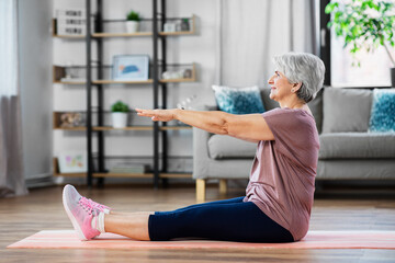 sport, fitness and healthy lifestyle concept - smiling senior woman exercising on mat with arms stretched forward at home
