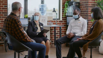 Therapist giving advice to multi ethnic group of people with face mask at aa meeting. Woman...