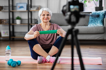 Fototapeta na wymiar fitness, sport and video blogging concept - happy senior woman or blogger with camera and resistance loop streaming online class at home