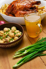 fried chicken meat and roasted potatoes on a white platter, a glass of beer, champignon mushrooms and green onions, delicious food on a wooden background