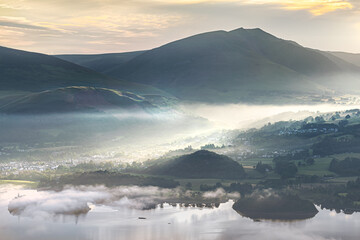 Morning elation as the sunrise illuminates Keswick in the English Lake District with rays of light streaming throught the early mist on the shore of Derwentwater