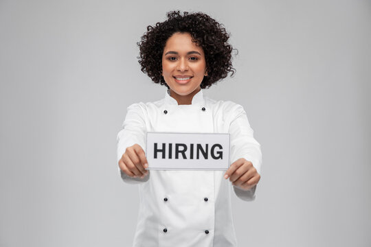 job, work and employment concept - happy smiling female chef in white jacket holding hiring sign over grey background
