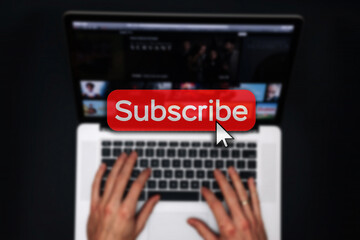 Subscribe now. Online video subscription red button. Internet service on laptop digital tablet blured technology background. Streaming video. Communication network.