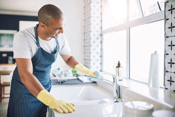 I like to see my reflection through my surfaces. Shot of a young man cleaning a kitchen at home.