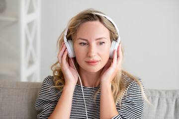 Pleasant music. Inspired woman. Stereo sound. Happy relaxed lady listening favorite song on headphones sitting sofa in light room interior.