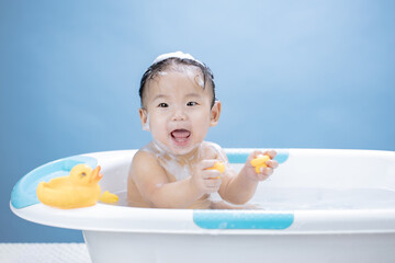 Baby having bath in tub and playing with Yellow Duck on blue background - 491398211