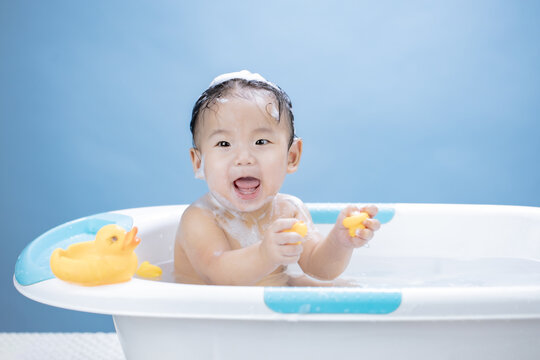 Baby having bath in tub and playing with Yellow Duck on blue background