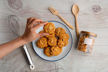 Hand and homemade almond cookies in ceramic white plate on wood table background.