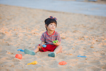 Little boy playing with beach toys on the sand in summer.