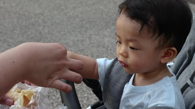 Asian Chinese 11month old baby eating snack while sit on troller at park.
