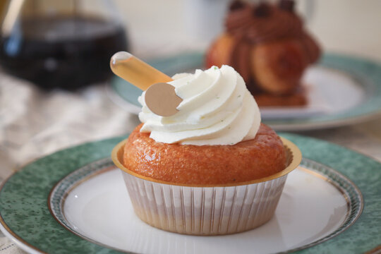 Close up of French baba au rhum topped with mousse white vanilla cream and a tube of rhum on it. It's a yeast dough sponge cake, baked in a ring mold, and soaked in rum. With coffee in background