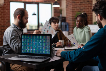 Diverse businesspeople discussing financial profit analyzing stock data during business meeting in startup office. Laptop computer with annual report on computer screen. Global economy
