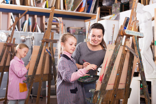 Positive female teacher correcting work of girl during painting class at art studio