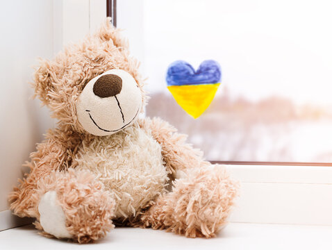 a teddy bear on the windowsill and a painted heart with the Ukrainian flag