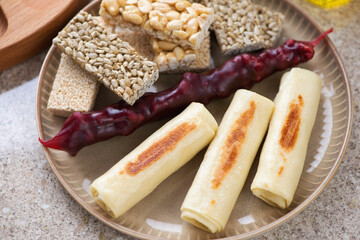 Beige plate with georgian stuffed crepes, churchkhela and kozinaki, middle close-up, selective focus