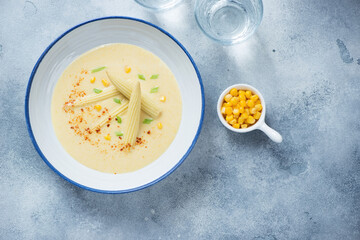 Plate of cream-soup made of baby corn over light-blue stone background, above view, horizontal shot with space
