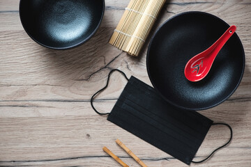 Black bowls with black protective face mask on a wooden table, top view, horizontal shot with space