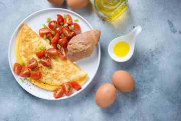 White plate with omelet and sliced cherry tomatoes, flat lay on a light-blue stone background, horizontal shot