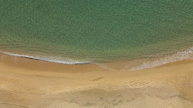 Top down view of a clear water beach in Spain with calm weaves rolling into coastline