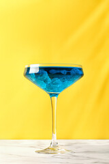 Glass of Iced blue hawaii or Blue lagoon cocktail on yellow background and marble table.