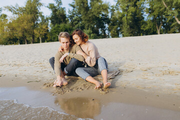 Fototapeta premium A loving couple has fun - they laugh, hug each other and enjoy a warm summer evening. Romantic couple sitting by the sea. Male and female legs on the beach. The guy draws on the sand. Heart