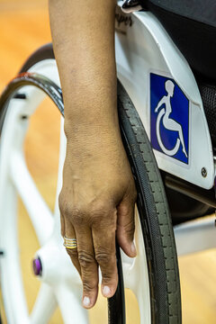 Detalhe da m&atilde;o de uma mulher com dificuldade de locomo&ccedil;&atilde;o sentada, segurando a roda da sua cadeira de rodas pronta para se mover.