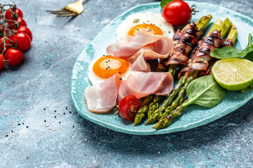 Ketogenic diet. Keto brunch breakfast. fried eggs, asparagus wrapped in bacon, ham, tomatoes and salad. Food recipe background. Close up