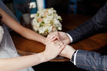 Obraz na płótnie Canvas bride and groom holding hands near boquet on a cafe