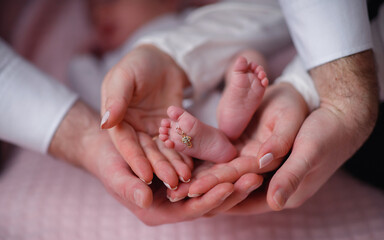 The hands of the mother and father are holding the little feet of the child in the palms, close-up...