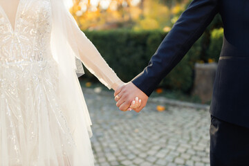 Bride and groom in a dark suit and white wedding dress holding hands on the background of a green...