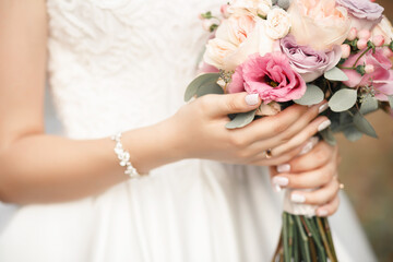 Obraz na płótnie Canvas A bride with a white classic manicure holds a wedding bouquet of white and roy roses in her hands