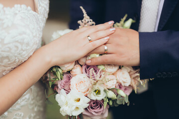 Bride and groom in black suit and wedding dress hold hands with gold wedding rings on a wedding...