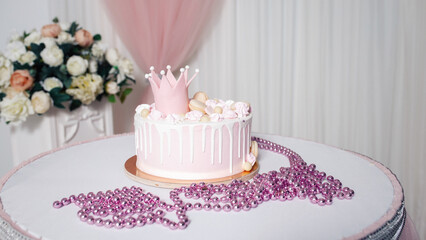 Big pink cake with cookies and a crown for a little girl for birthday on the table with glittering beads