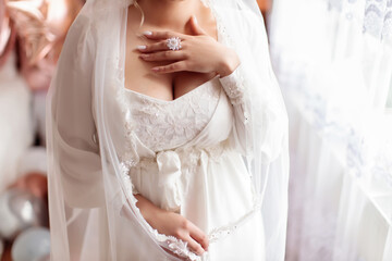 A young girl bride with big breasts in a white peignoir and a veil put her hand on her heart