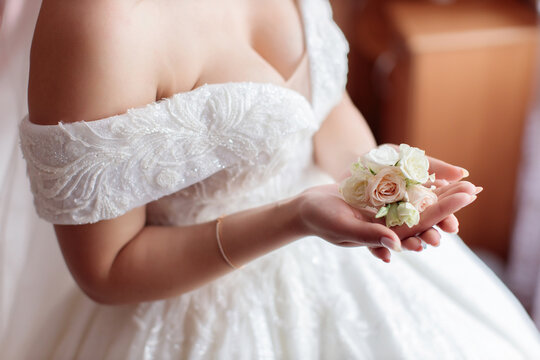 A young girl bride with big breasts in a white wedding dress and with a veil put her hands with a manicure on her neck