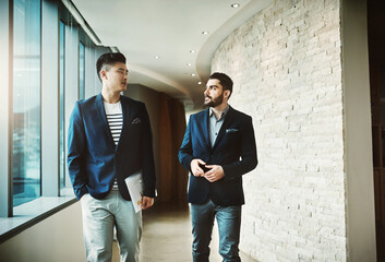 Success is all about the nows and tomorrows. Shot of two young businessmen walking and talking in a...