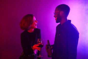 Minimal waist up portrait of young couple laughing while enjoying party in neon light