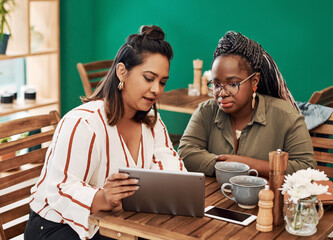Girly catch ups arent complete without a good browsing session. Shot of two young women using a digital tablet together at a cafe.